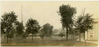 Fotografía horizontal en sepia que muestra un grupo de edificios de ladrillo bordeando un espacio verde abierto con árboles dispersos. Algunos de los edificios de ladrillo parecen ser casas de Carl Michel